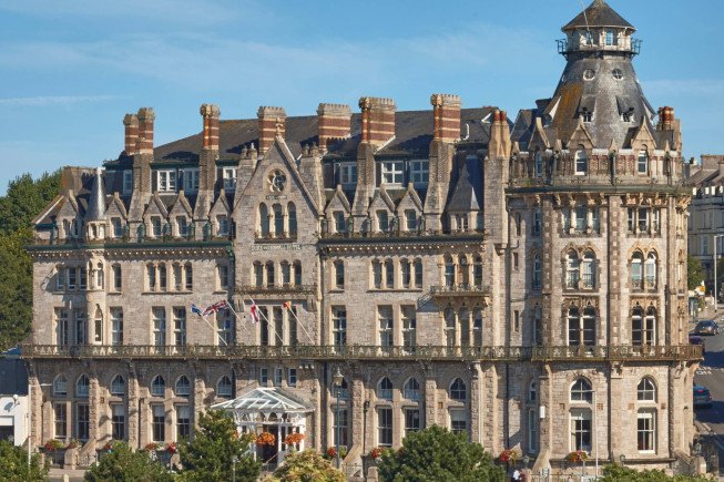 Large ornate stone building with many windows, steep roofs, and a tower against a blue sky.