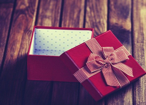 An open red gift box with a lid topped by a bow, sitting on a wooden surface.