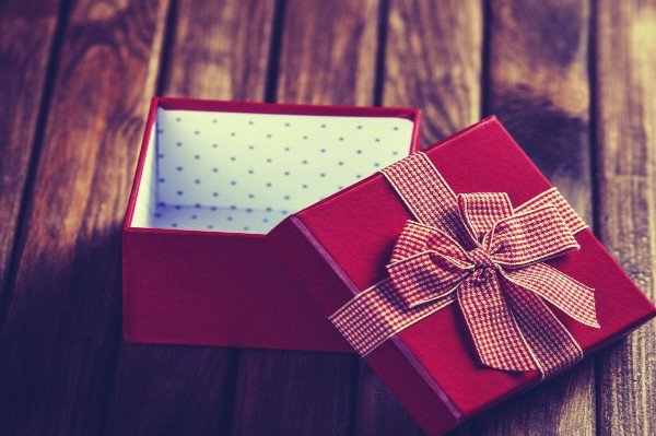 An open red gift box with a patterned ribbon on the lid sits on a wooden table.