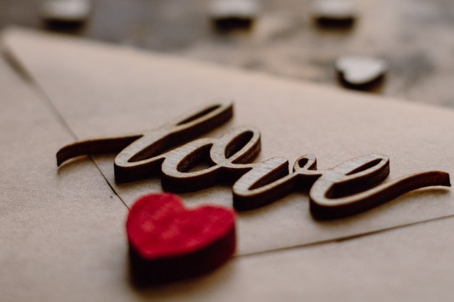 Close-up of a wooden cursive word "love" with a small red heart beside it on a light background.