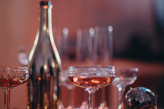 A table setting with several champagne coupe glasses, a tall bottle, and a small disco ball in warm lighting.