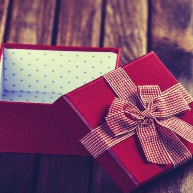 An open red gift box with a patterned ribbon on the lid sits on a wooden table.