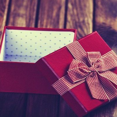 An open red gift box with a patterned ribbon on the lid sits on a wooden table.