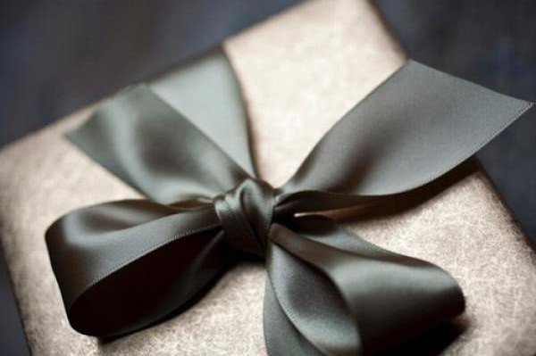 A wrapped gift box with a dark satin ribbon tied into a bow on top.