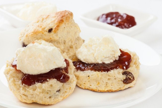 Three scones topped with jam and dollops of cream on a white plate.
