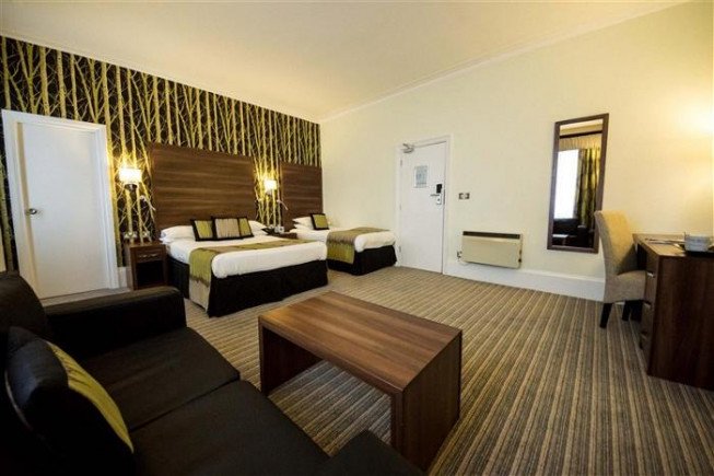A hotel room with two beds, a sofa, a coffee table, a desk, and a wall mirror.