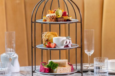 A three-tier dessert stand holding assorted cakes and pastries, surrounded by glasses on a table.