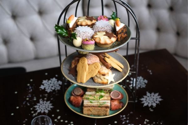 A three-tier stand filled with assorted pastries, cookies, and sweets on a table with snowflake decorations.