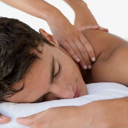 Close-up of a person lying face down while another person’s hands massage their shoulders.