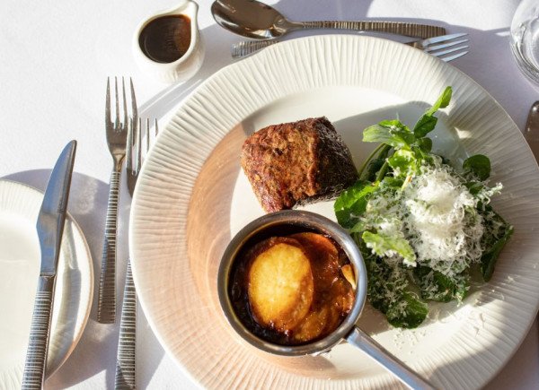 Overhead view of a plated meal with a piece of meat, a small pan of sauce or mashed potato, and a green salad topped with grated cheese.