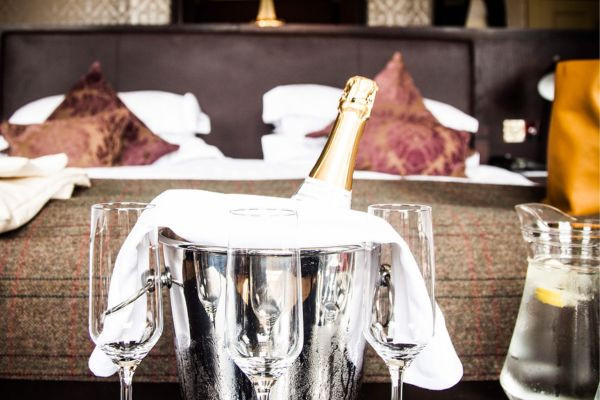 A bottle of champagne in an ice bucket surrounded by empty glasses on a table in a hotel room.
