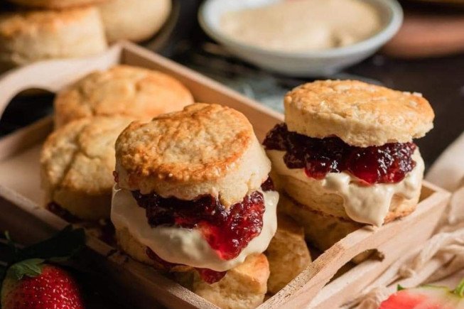 Tray of shortcake biscuits filled with cream and berry jam, with strawberries in the foreground.