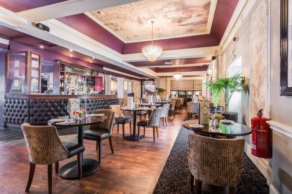 An elegant lounge with tables and chairs, a bar area, warm lighting, and wood flooring.