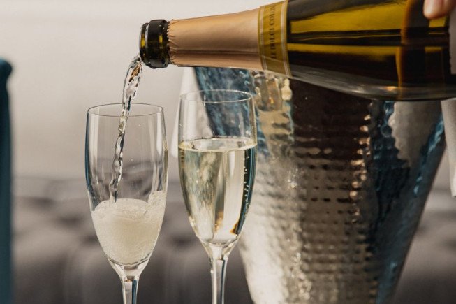 A bottle pours sparkling wine into a champagne flute beside another filled glass.