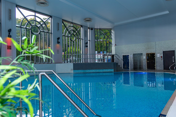 An indoor swimming pool with blue water, metal handrails, and tall arched windows along one wall.