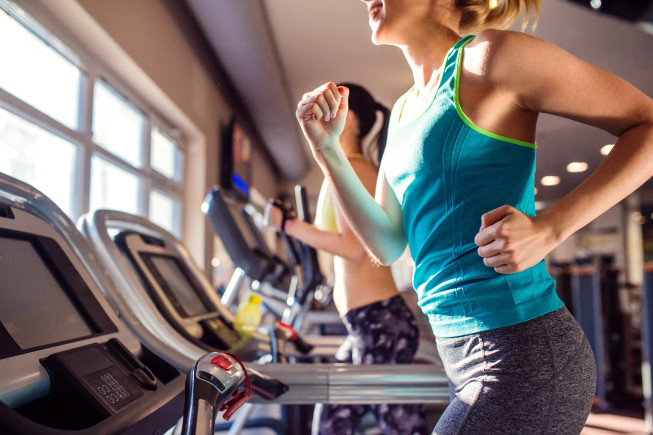 Two people jogging on treadmills in a fitness center, with a close-up of one runner in the foreground.