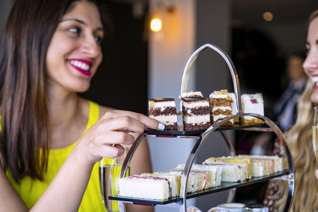 Two women looking at and choosing small layered cakes on a tiered dessert stand.