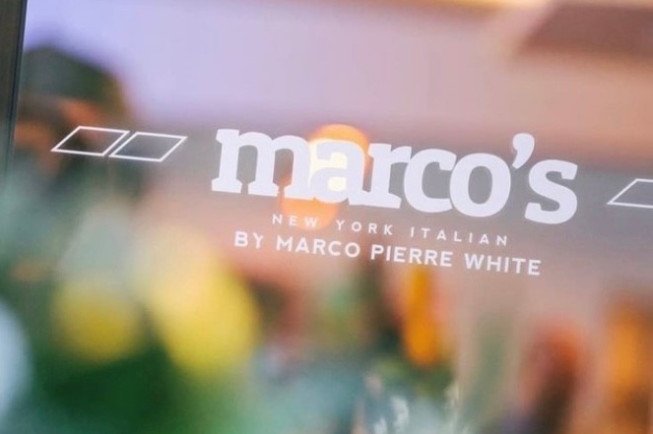 Blurred storefront sign reading “marco’s” with smaller text “new york italian by marco pierre white.”