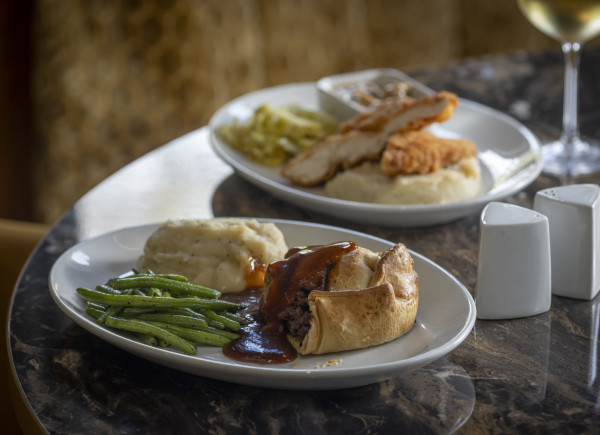 Two white plates with meat pie or pastry, mashed potatoes, green beans, gravy, and other side dishes on a restaurant table.