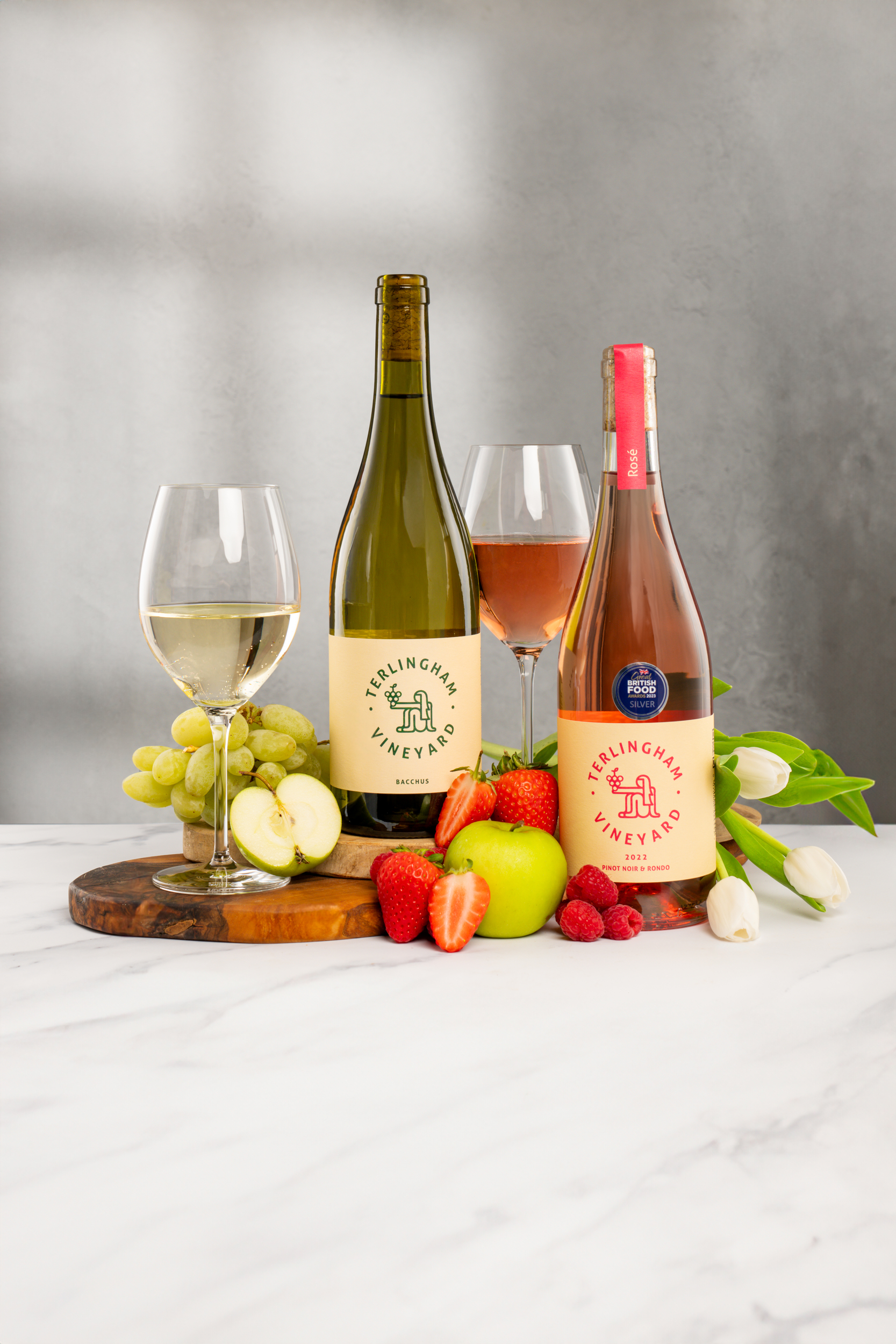 Two bottles of wine with glasses and fresh fruit on a marble surface