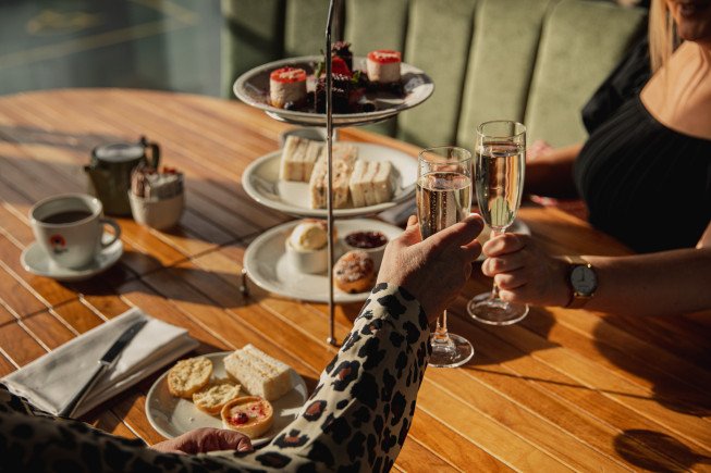Two people toasting with champagne flutes over a table of treats