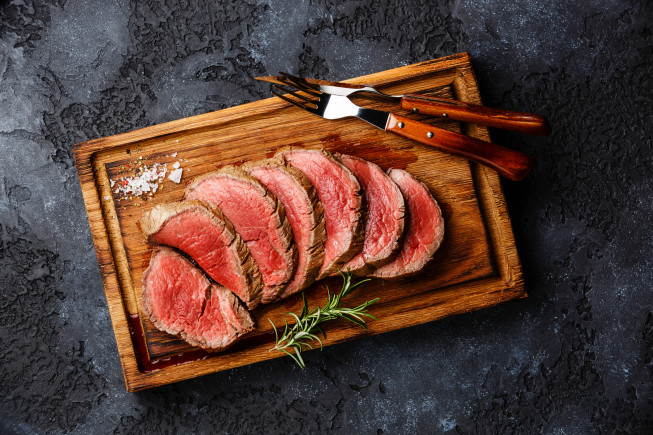 Sliced roast beef arranged on a wooden cutting board