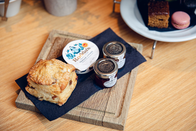 A freshly baked scone served with cream and jam on a wooden board