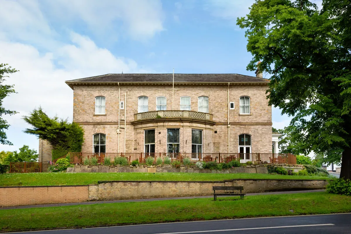 A historic brick building surrounded by greenery and a bench.