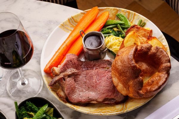 A plate of roast beef, vegetables, and a glass of red wine.