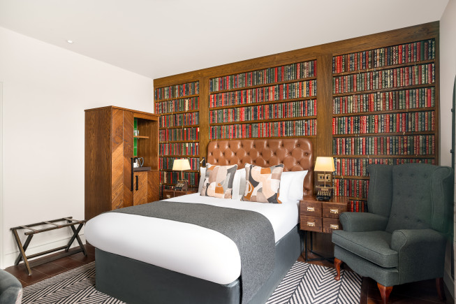 Stylish hotel room featuring a large bed and bookshelf wall