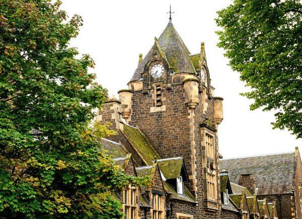 Clock tower of a historic stone building surrounded by trees